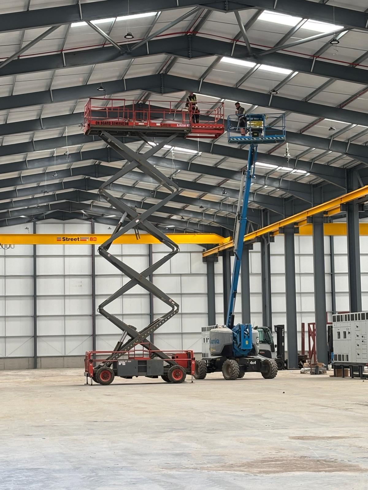 Electricians on scissor lifts installing high bay lighting in a warehouse roof